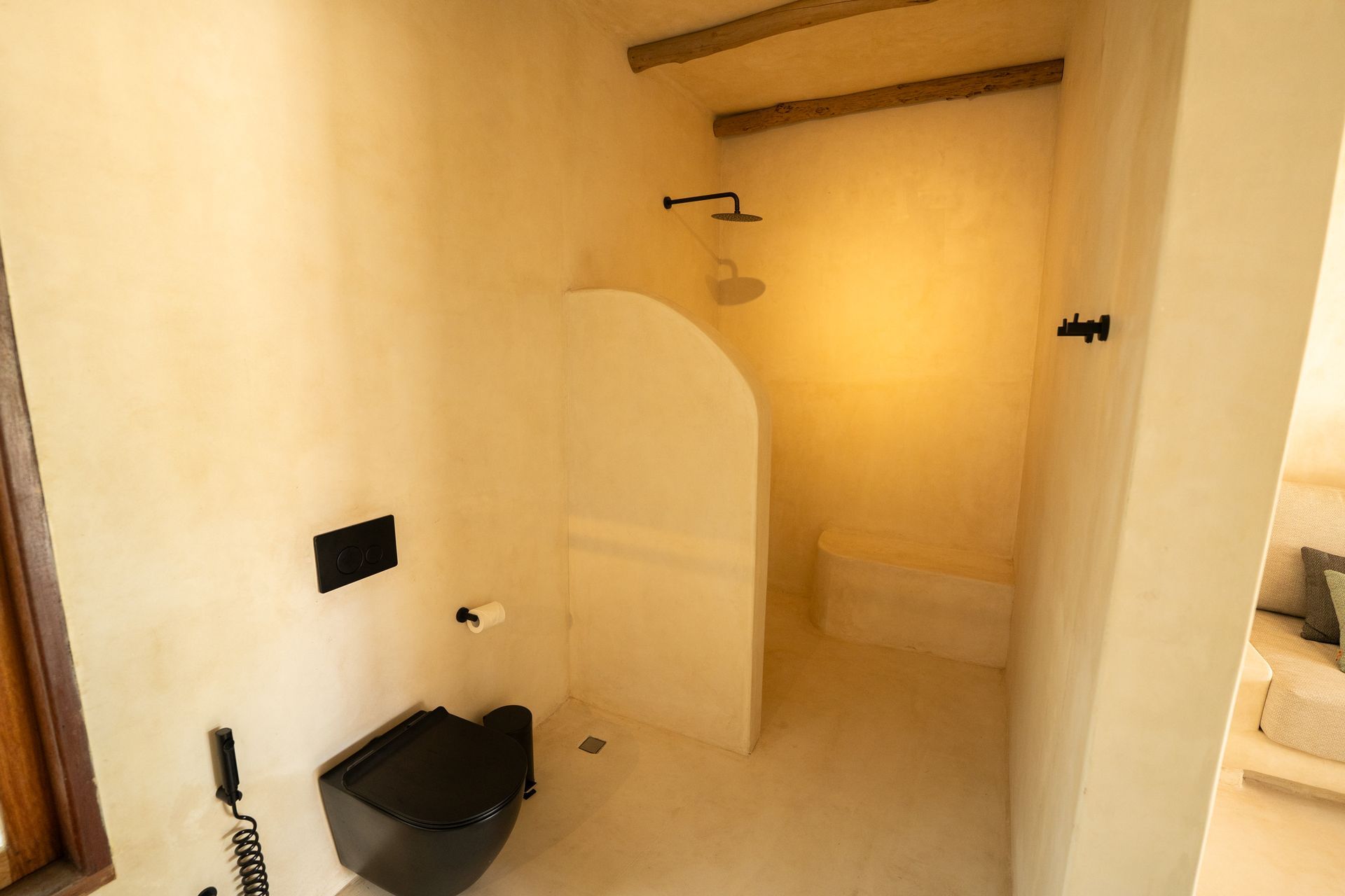 Bathroom with beige walls and a black toilet. Includes a shower, a towel rack, and wooden beams on the ceiling.