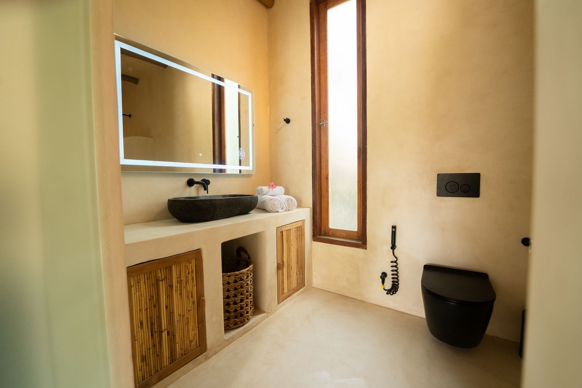 Bathroom with a black sink, toilet, and a large lighted mirror; neutral colors, wooden cabinets.