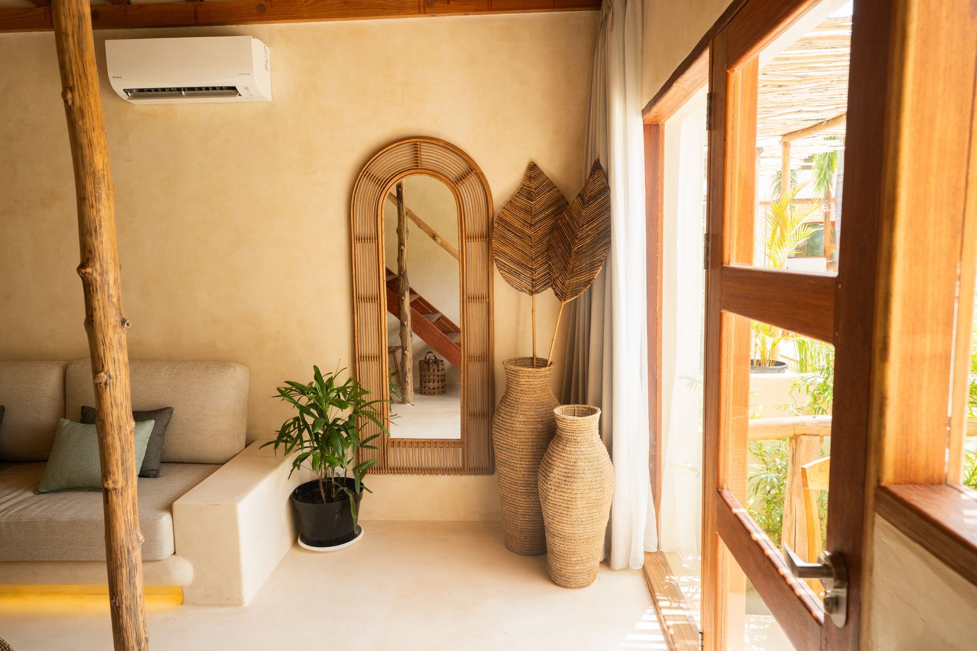 Beige living room with wicker mirror, woven vases, and open door to a balcony.