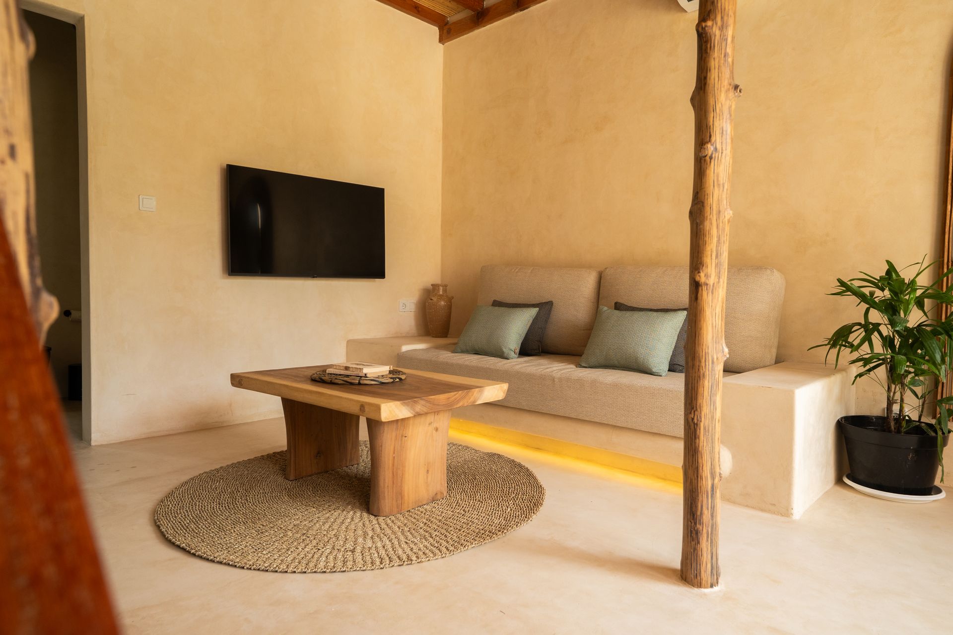 Cozy living room with a beige sofa, wooden table, mounted TV, and a round rug.
