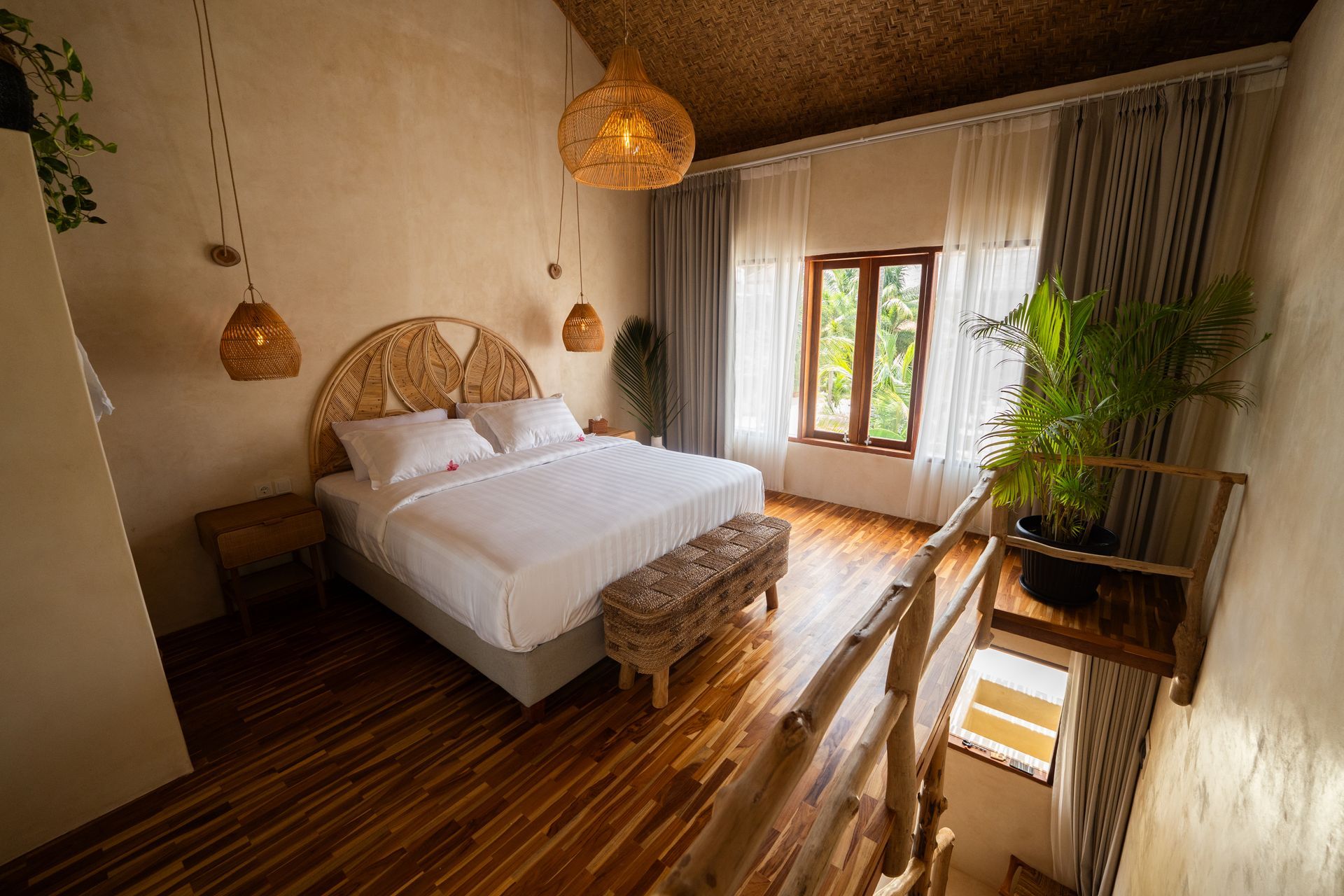Bedroom with wooden floor and headboard. Hanging lamps, large window, and plants create a cozy atmosphere.