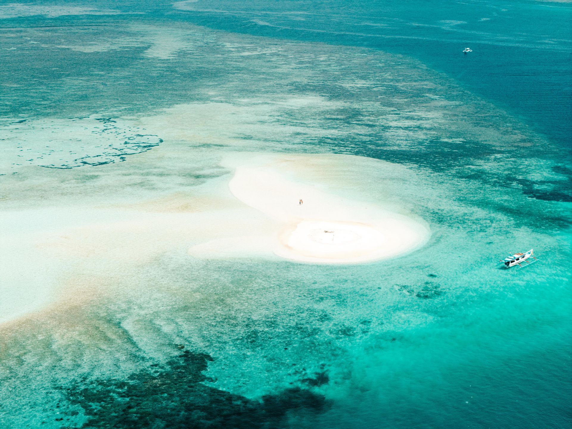 Aerial view of a sandbar in turquoise water with a boat and some people.