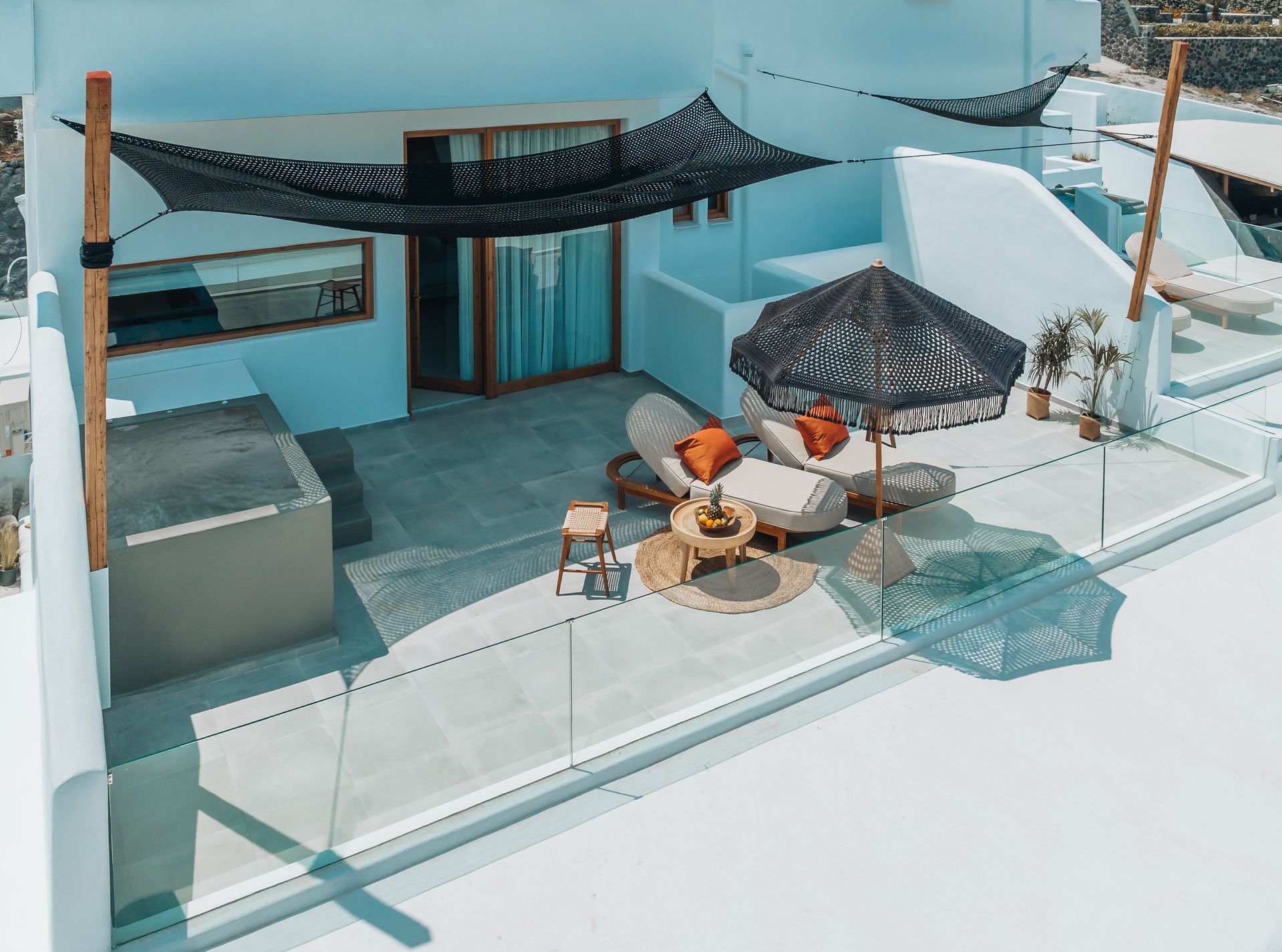 Rooftop terrace with white walls, lounge chairs, a black umbrella, and ocean views.