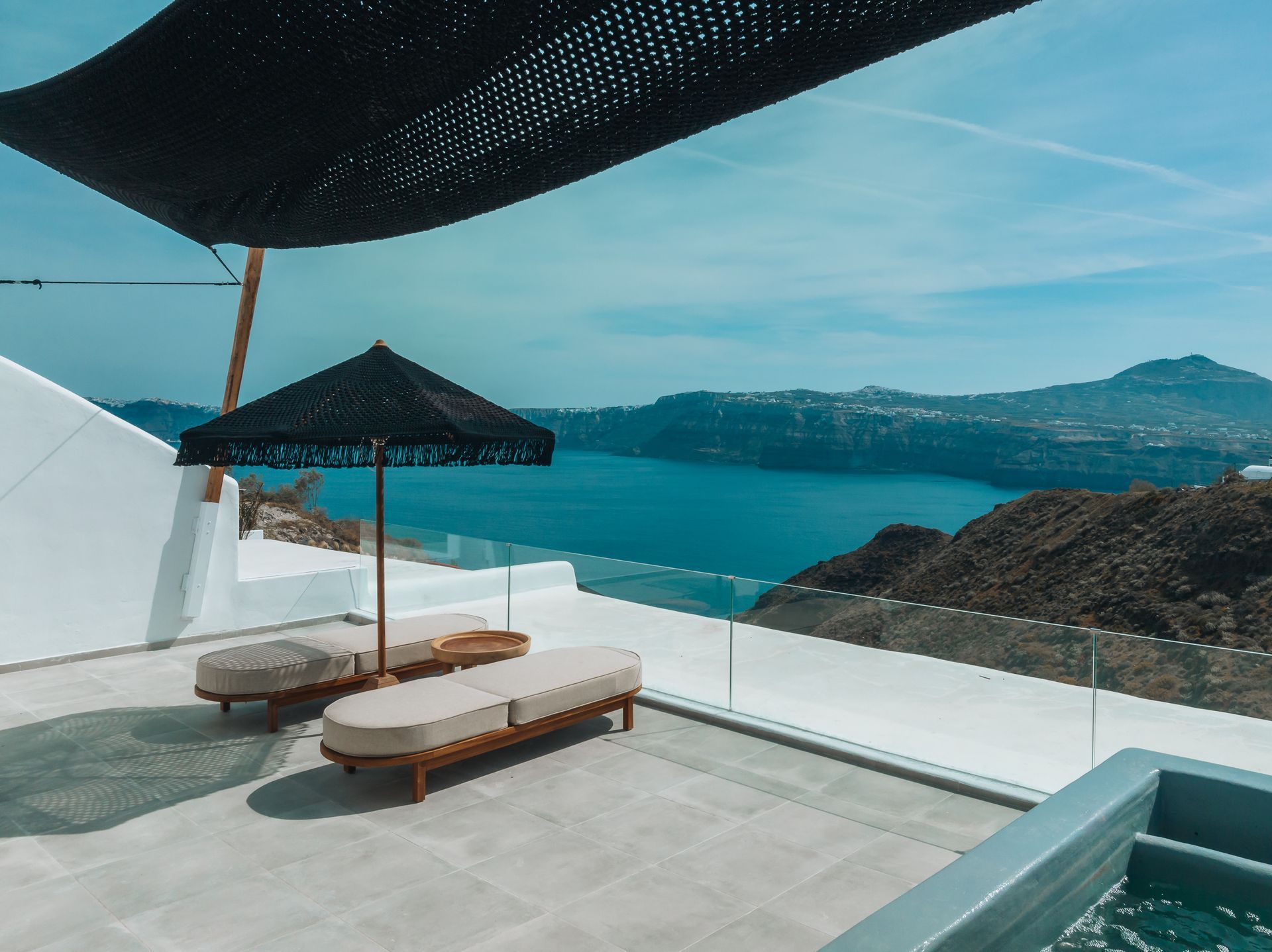 Terrace with ocean view in Santorini. Lounge chairs under black umbrellas, white buildings.