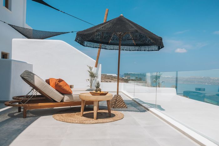 Rooftop terrace with lounge chairs, umbrella, and sea view under a blue sky