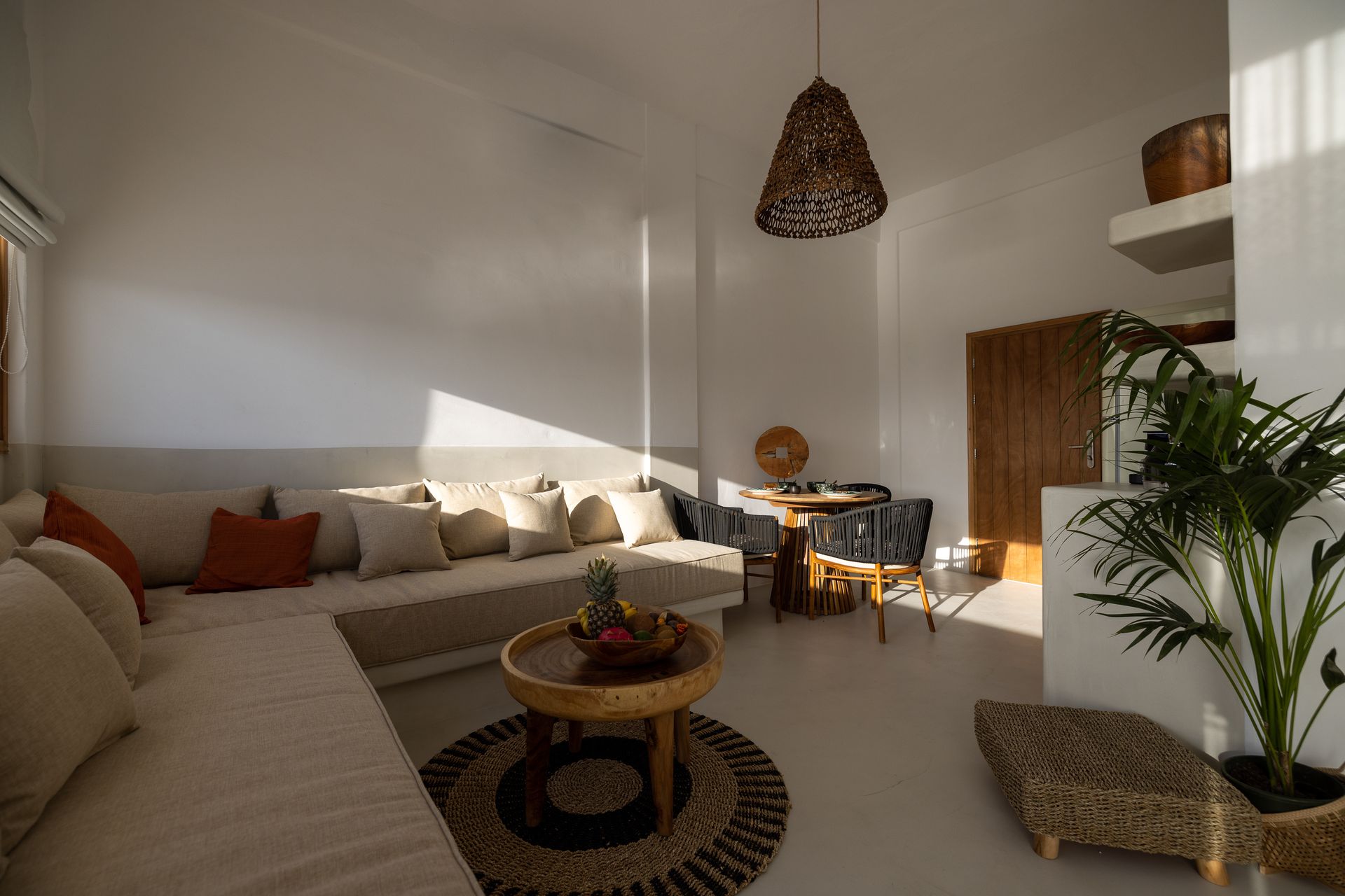 Bright living room with white walls, beige sofa, wooden table, and woven accents.