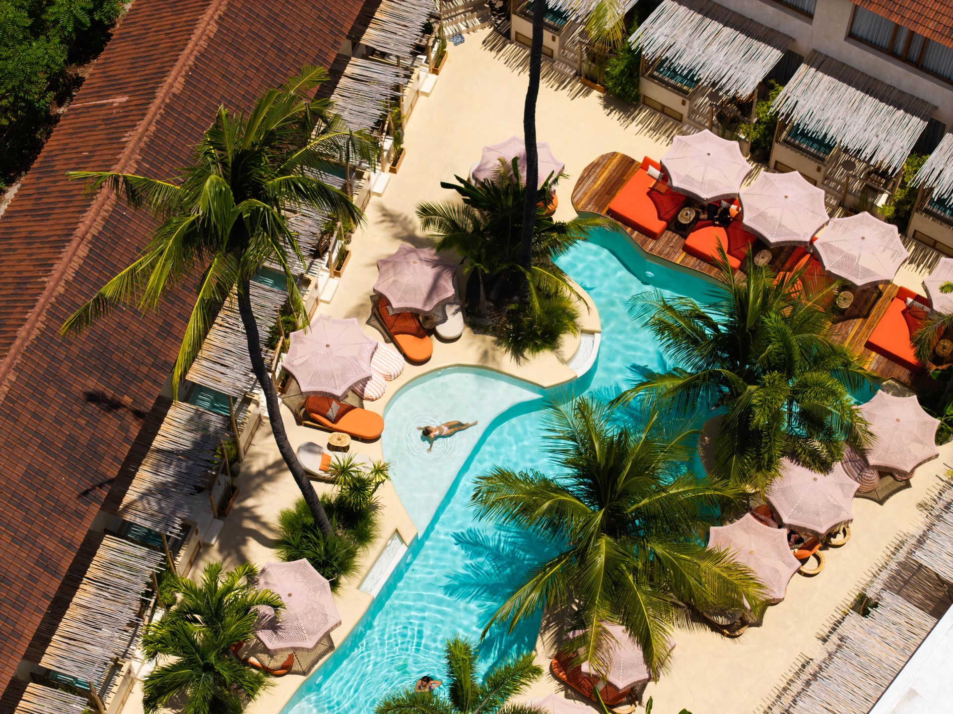 Aerial view of a pool with palm trees, lounge chairs, and a person swimming.