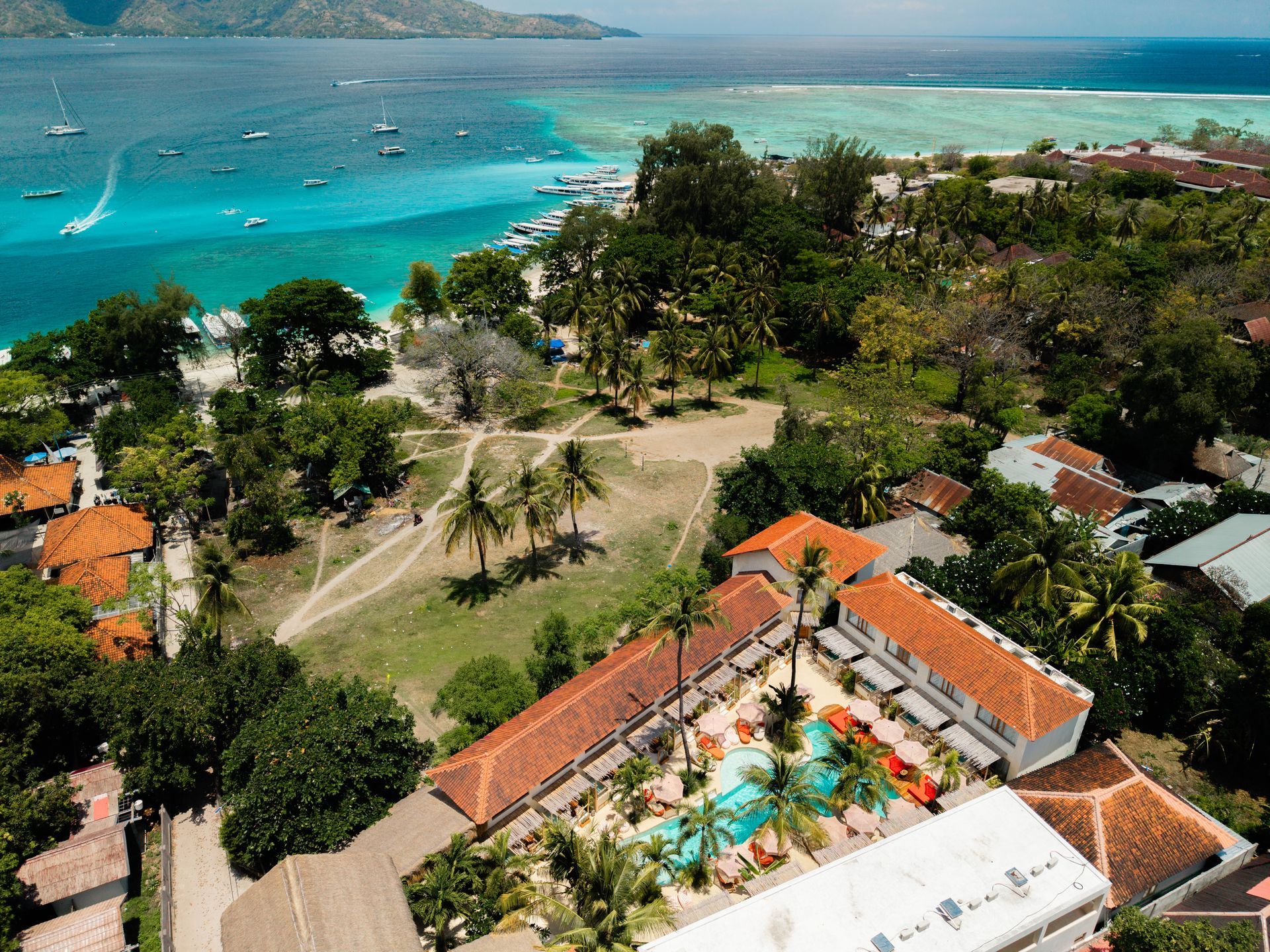 Aerial view of a tropical resort with a turquoise ocean, boats, and green trees.