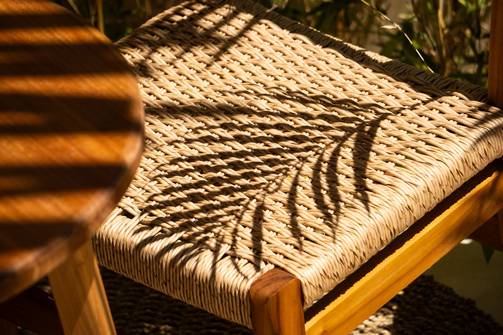 A wooden chair with woven seat, palm leaf shadow.