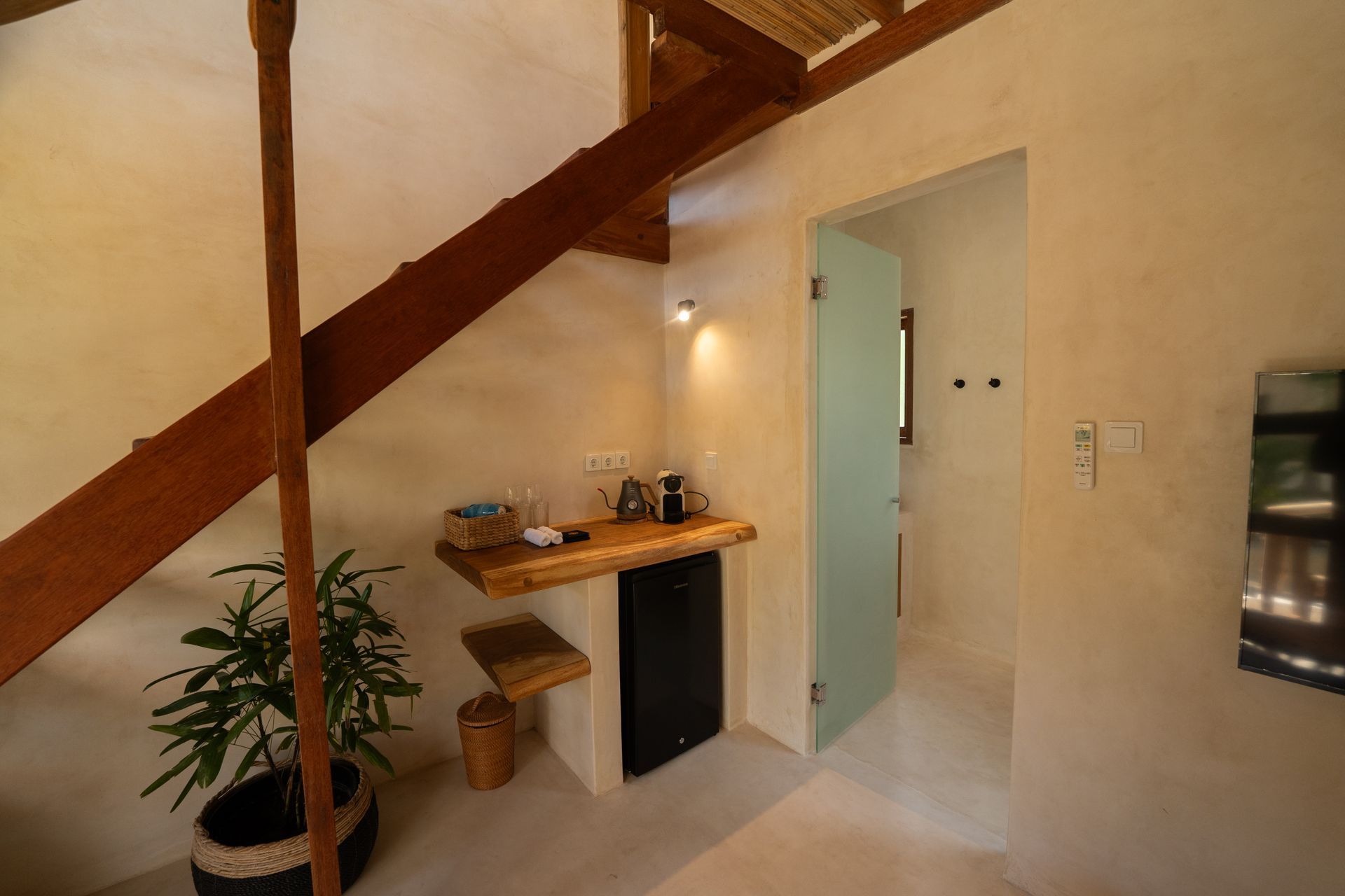 Interior of a room with a wooden staircase, small kitchen area, and a glass door leading to a bathroom.