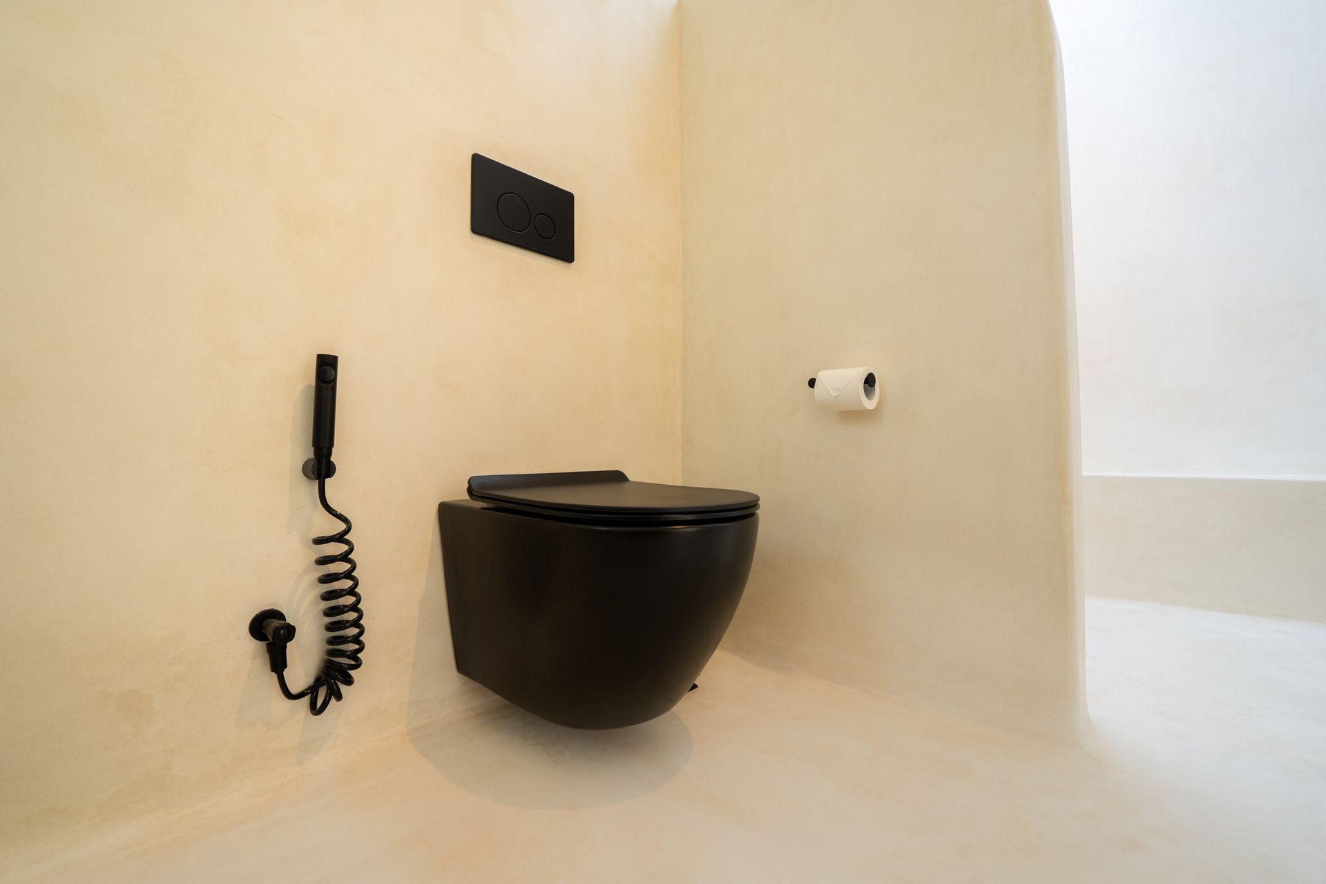 Black toilet in a white bathroom, with a bidet sprayer on the left. Minimalist design.
