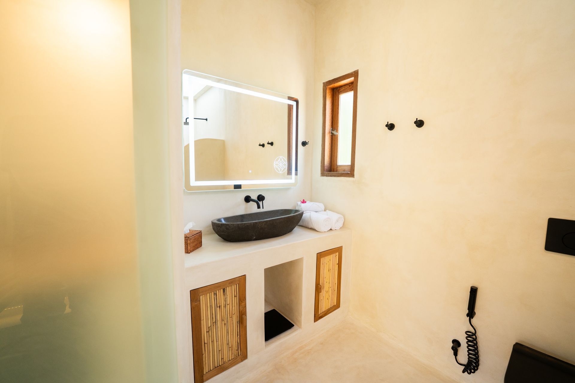 Bathroom with stone sink, lit mirror, wood accents, and frosted glass shower door.