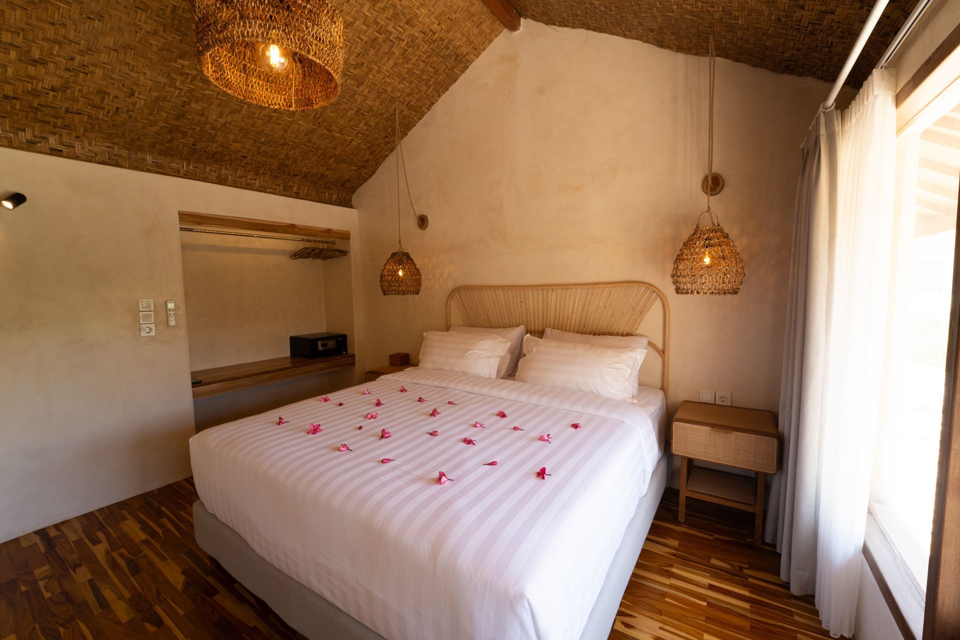 Bedroom with a queen bed, straw ceiling, white walls, and wooden furniture. Petals on the bed.