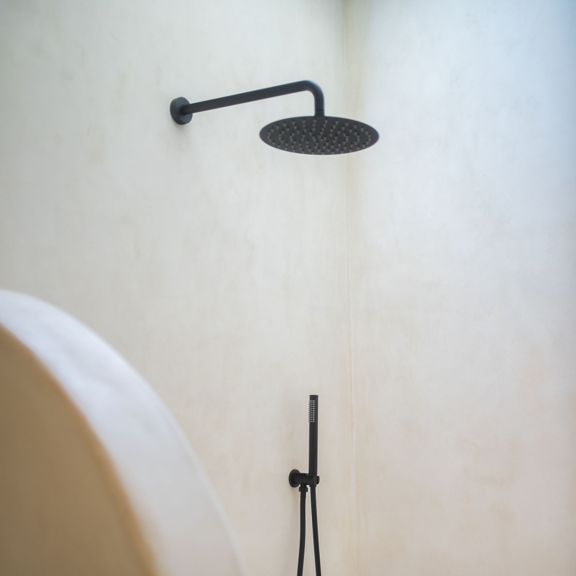 Black shower head and handheld shower on a cream-colored wall in a shower stall.
