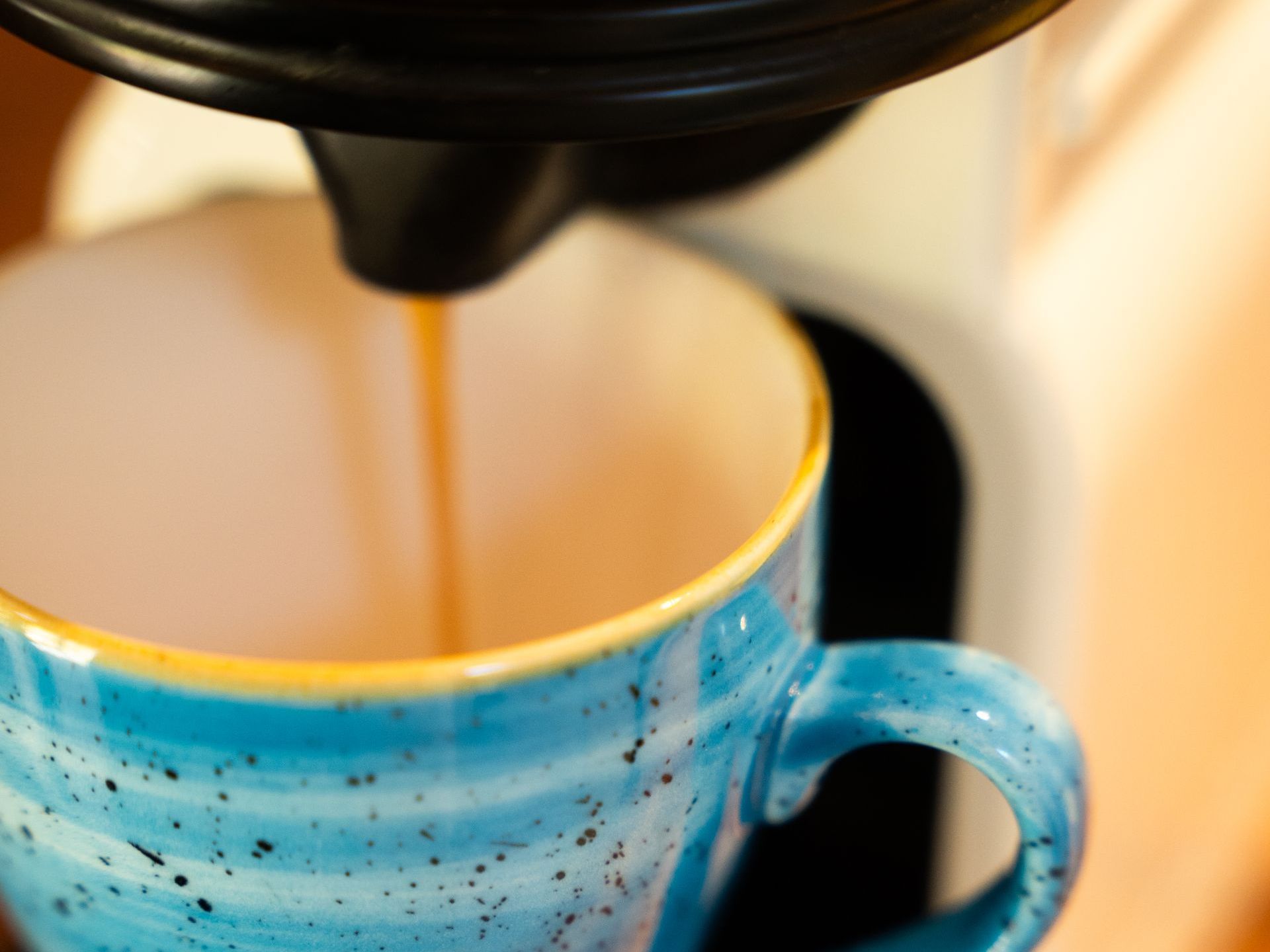 Coffee being brewed into a blue speckled mug from a white and black machine.