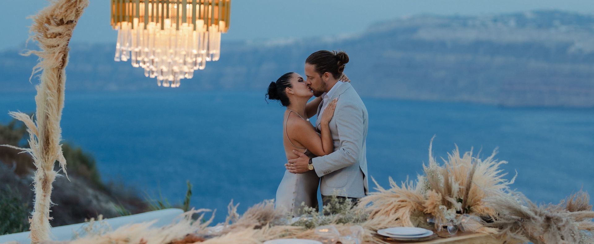 Couple kissing under chandelier, overlooking the sea.
