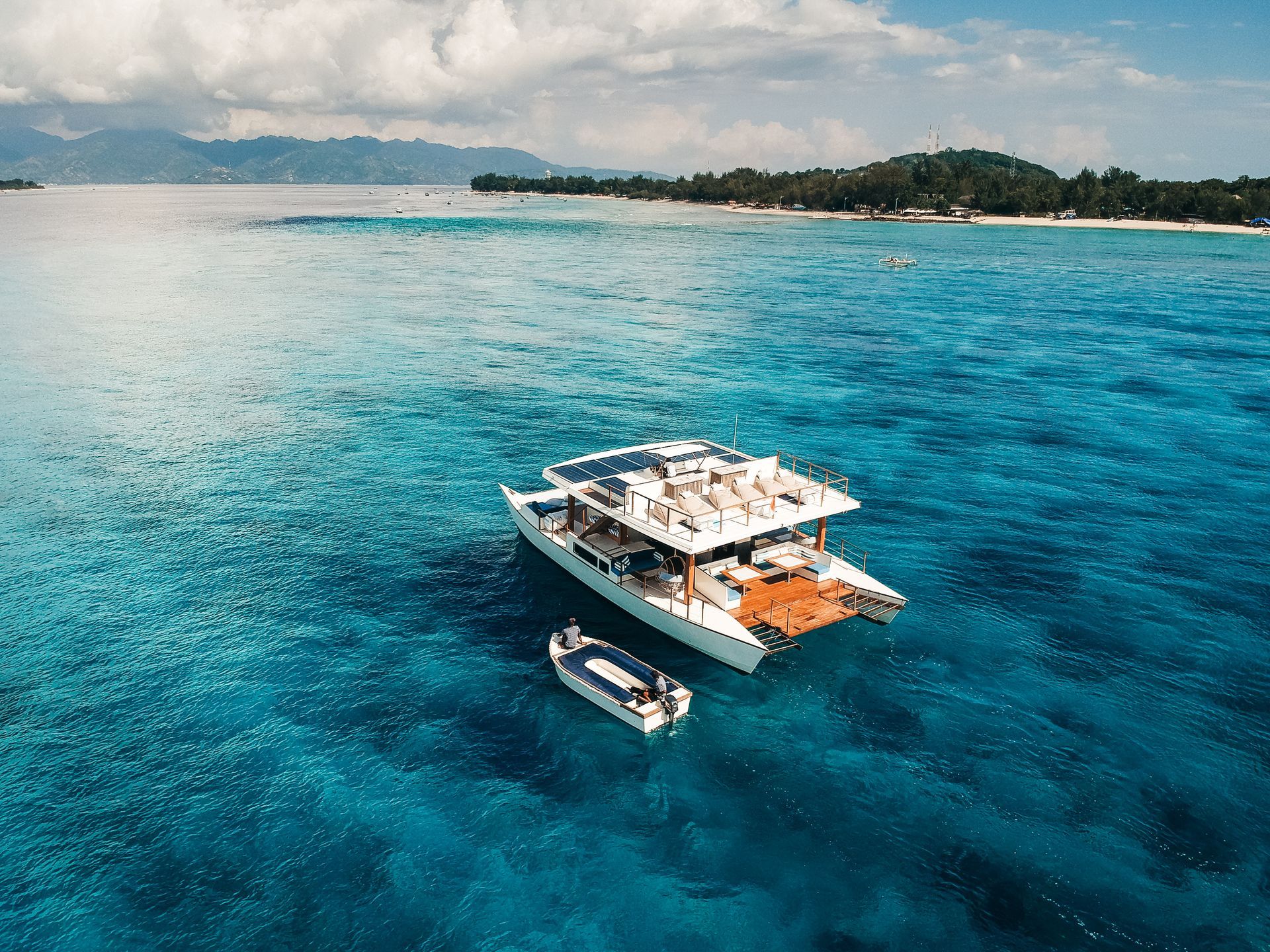 Catamaran boat in clear turquoise water; tropical island in background.