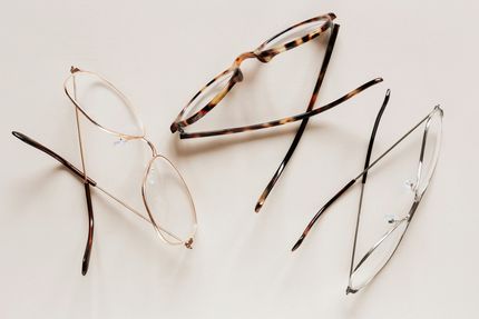 Three pairs of eyeglasses with open arms, scattered on a white surface. One pair is tortoiseshell.