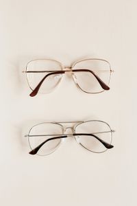Two pairs of eyeglasses with wire frames, one gold and one silver, on a beige surface.