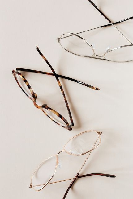 Three pairs of eyeglasses, one tortoiseshell, one silver, and one gold, arranged on a light-colored surface.