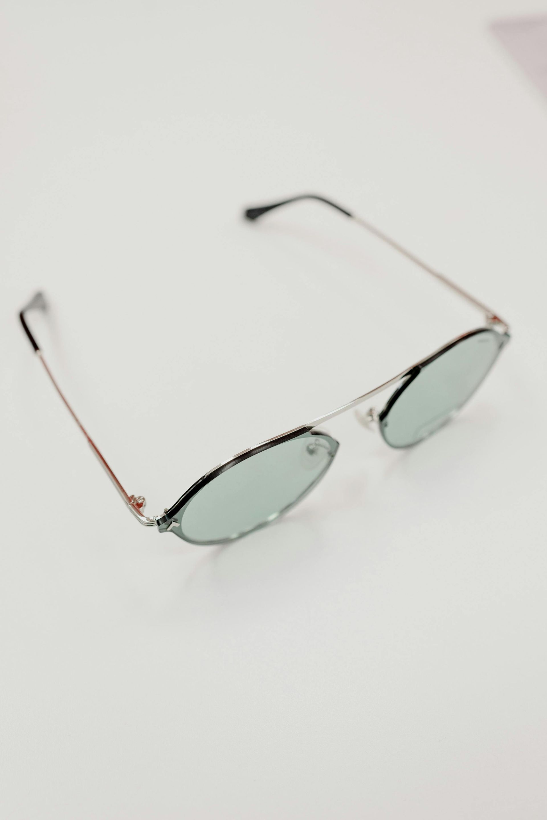 Silver-framed sunglasses with light green lenses on a white background.