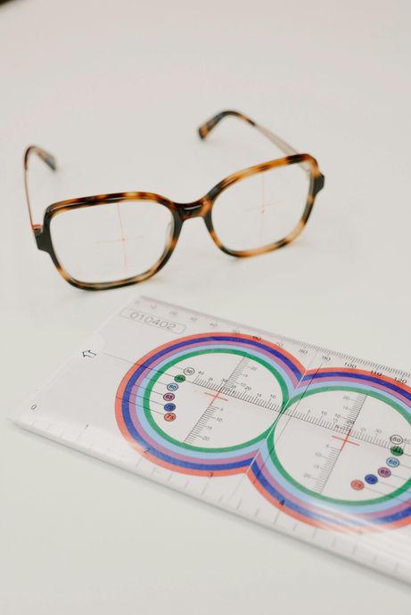 Tortoiseshell glasses sit above an eye chart ruler on a white surface.