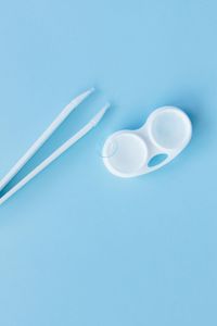 White contact lens case and tweezers on a light blue background.