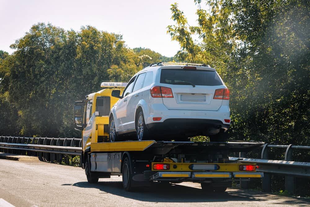 A White SUV Is Being Towed By A Tow Truck On A Highway — Wilson's Towing In Withcott, QLD