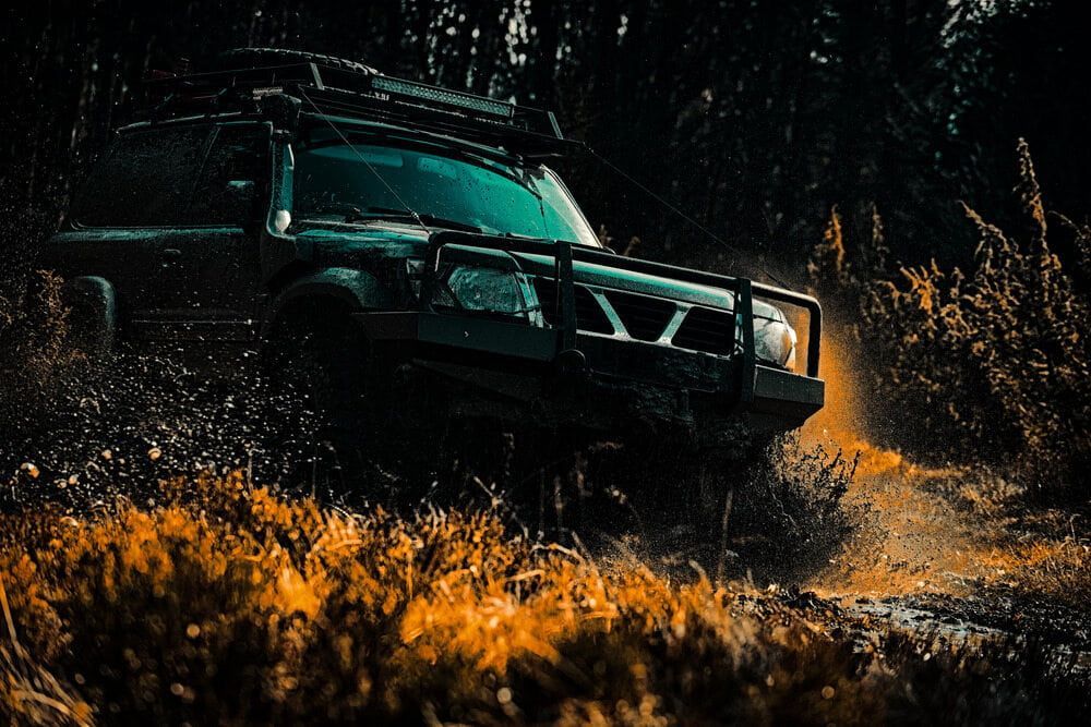 A Jeep Is Driving Through A Muddy Field In The Woods — Wilson's Towing In North Toowoomba, QLD