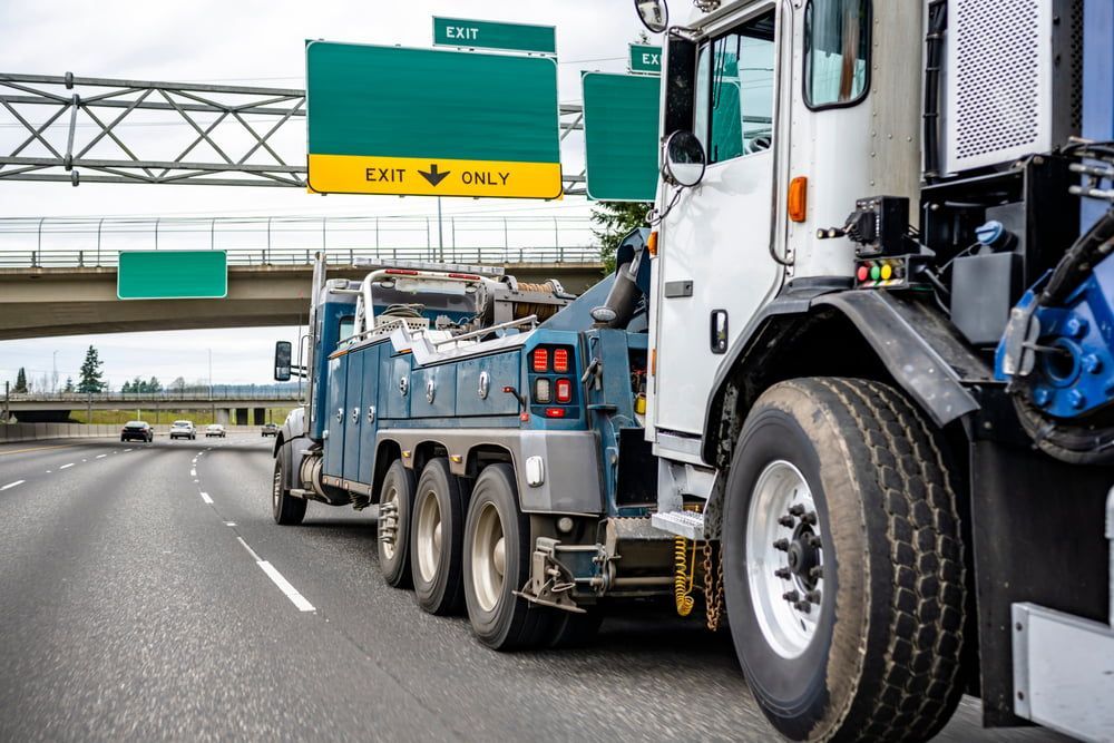 A Tow Truck Is Driving Down The Highway Next To Another Truck — Wilson's Towing In Gympie, QLD