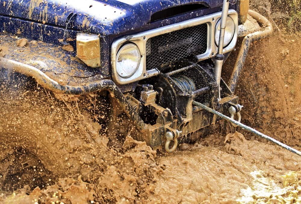 A Blue Jeep Is Stuck In The Mud With A Winch Attached To It — Wilson's Towing In Miles, QLD