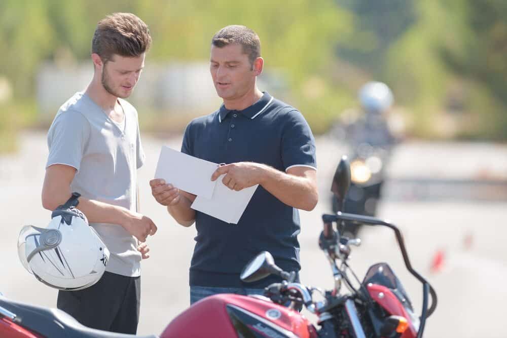 Two Men Are Standing Next To A Motorcycle And Looking At A Piece Of Paper — Wilson's Towing In North Toowoomba, QLD