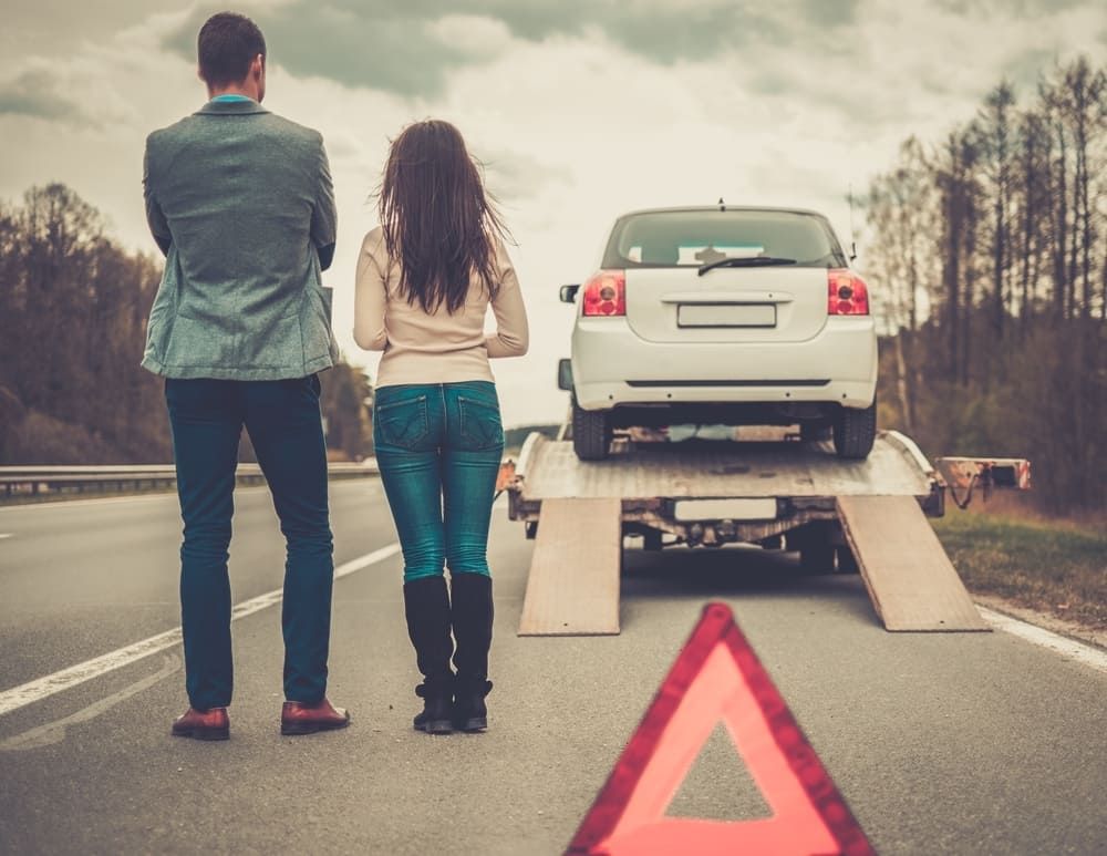 A Man And A Woman Are Standing Next To A Tow Truck With A Car On It — Wilson's Towing In Oakey, QLD