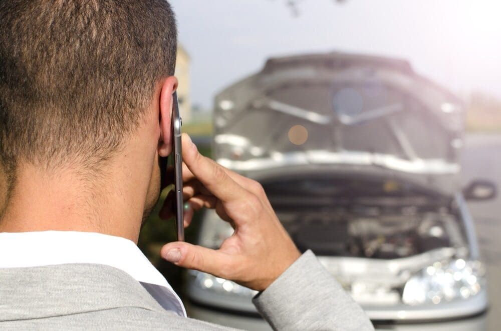 A Man Is Talking On A Cell Phone In Front Of A Broken Down Car — Wilson's Towing In Miles, QLD