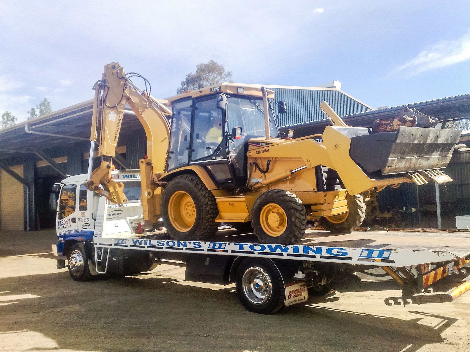 A Tow Truck Is Carrying A Yellow Tractor — Wilson's Towing In North Toowoomba, QLD