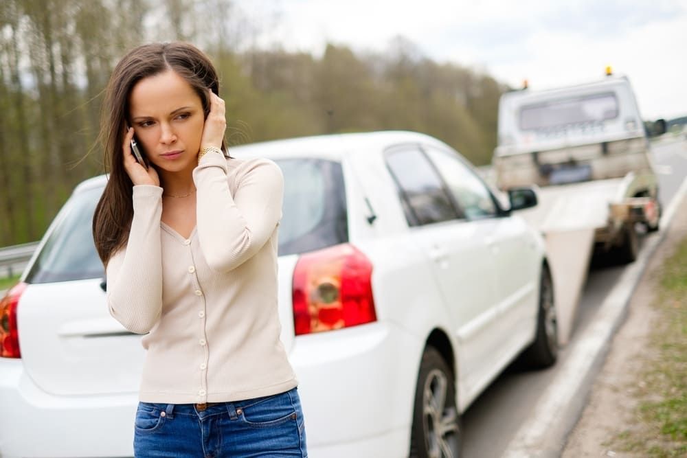 A Woman Is Talking On A Cell Phone Next To A Broken Down Car — Wilson's Towing In Oakey, QLD