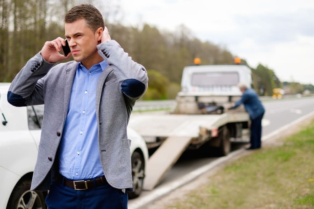 A Man Is Talking On A Cell Phone Next To A Tow Truck — Wilson's Towing In North Toowoomba, QLD