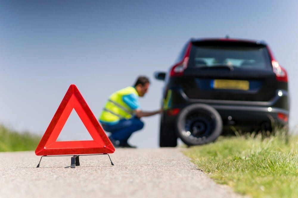A Man Is Changing A Tire On A Car On The Side Of The Road — Wilson's Towing In North Toowoomba, QLD