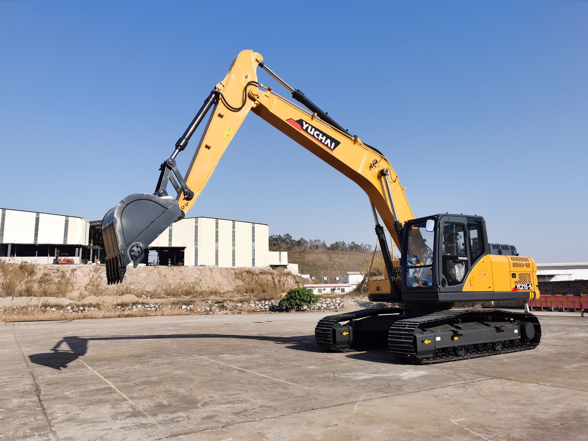 Yellow YUCHAI YC215 excavator on tracks lifting a silver bucket; blue sky background.