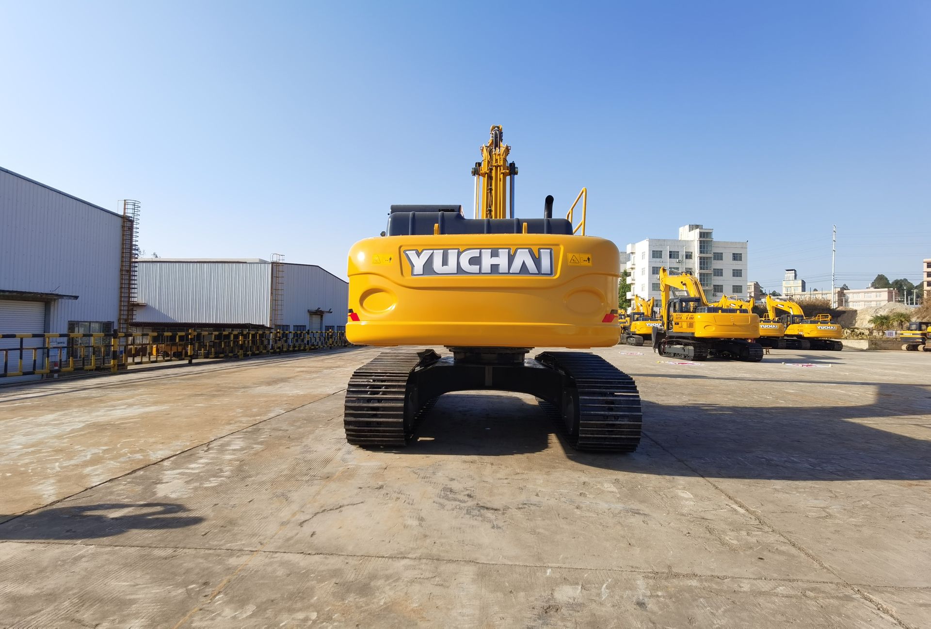Yellow YUCHAI YC215 excavator on a concrete lot, other machinery visible in background.