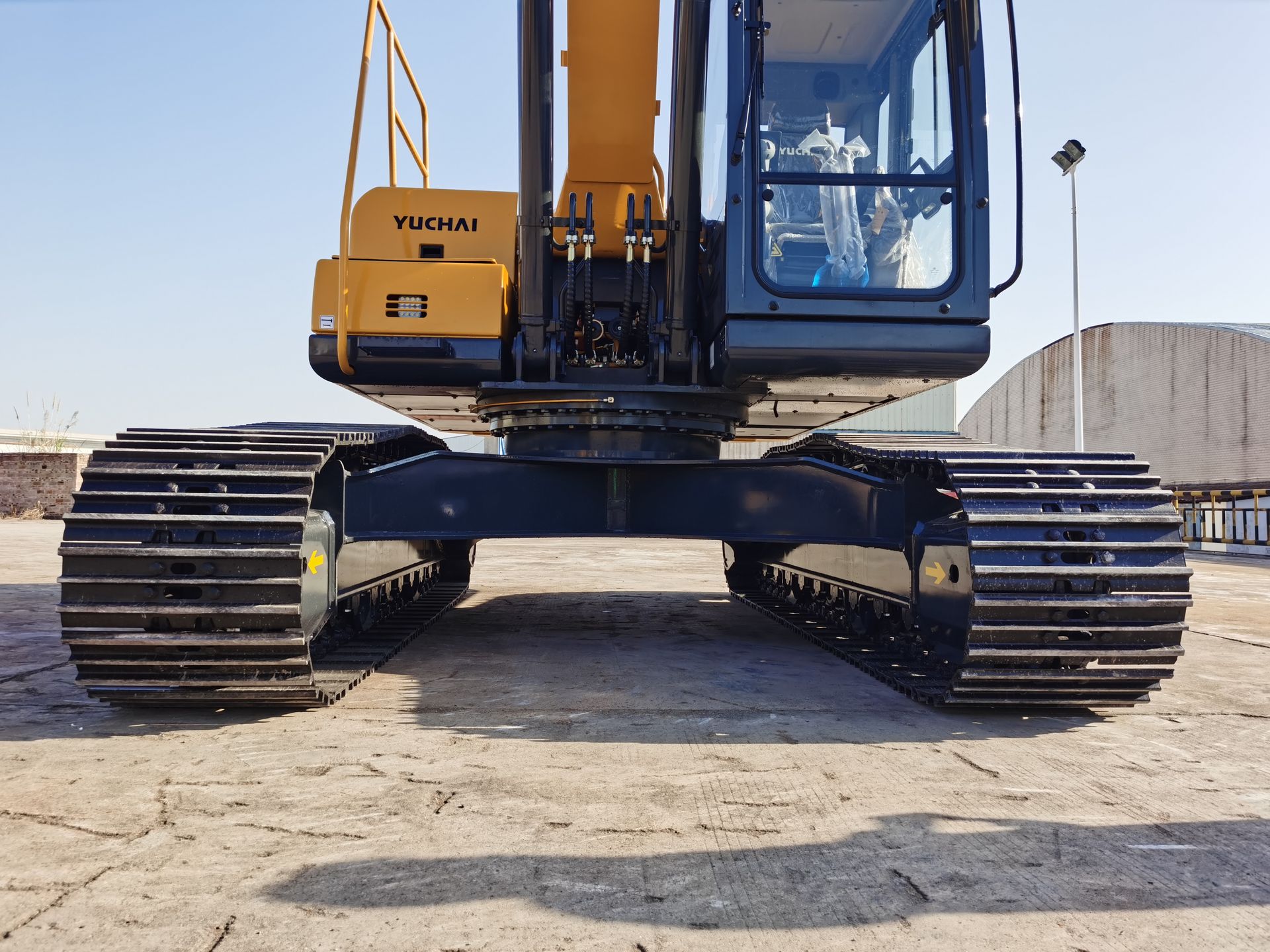 Yellow YUCHAI YC215 excavator tracks on a concrete surface, view from the front, with cab and boom visible.