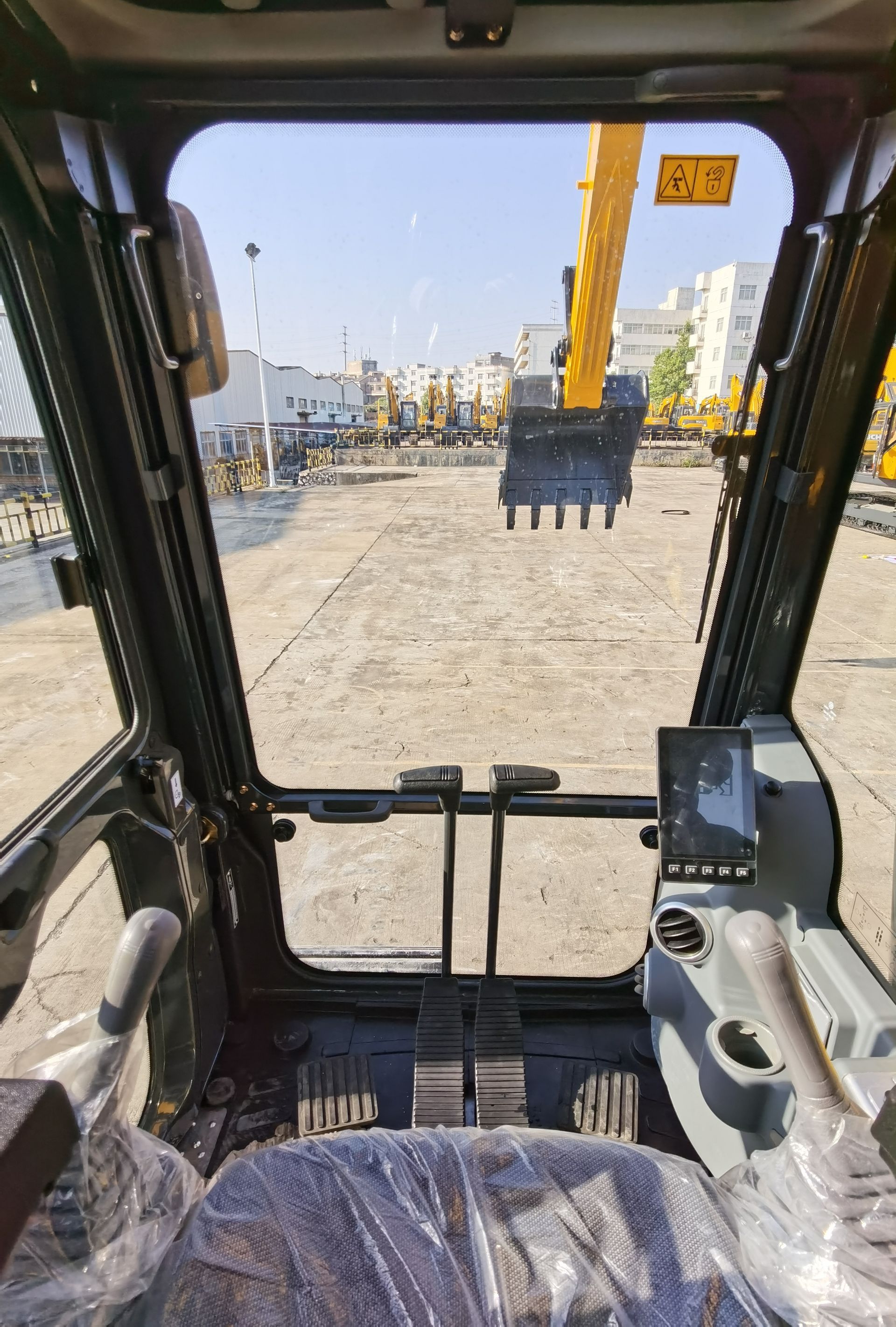 Inside YUCHAI YC215 excavator cab looking out at construction site and a yellow excavator.