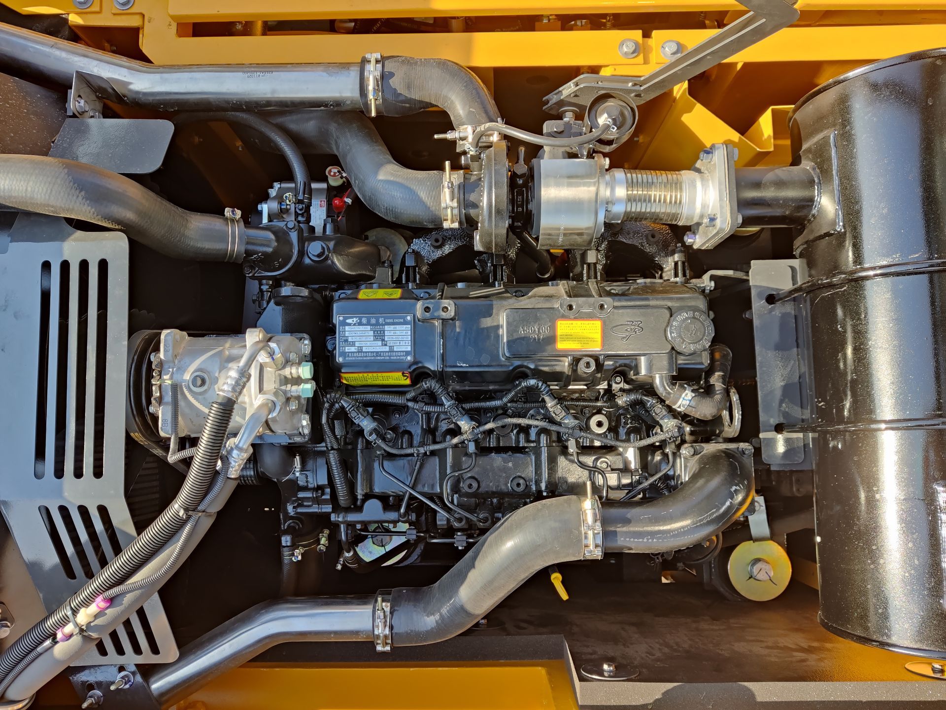 Black YUCHAI YC215 diesel engine with attached components inside yellow construction equipment.