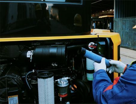 Person in blue overalls replacing an air filter on yellow YUCHAI construction equipment.