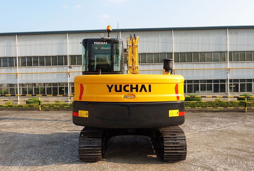 Yellow YUCHAI YC80 excavator, black tracks, against a factory background.
