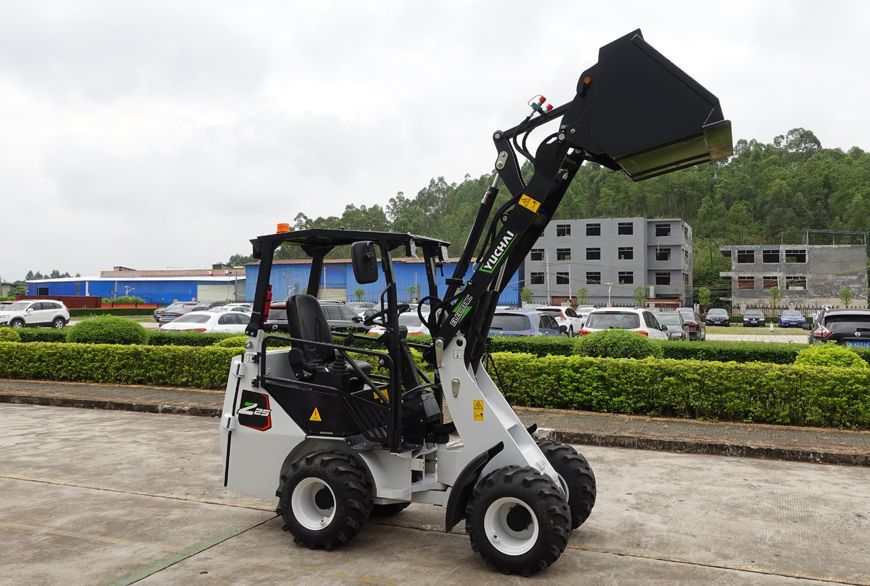 YUCHAI Z25 Compact gray front-end loader with bucket raised, parked outdoors near a hedge and parked vehicles.