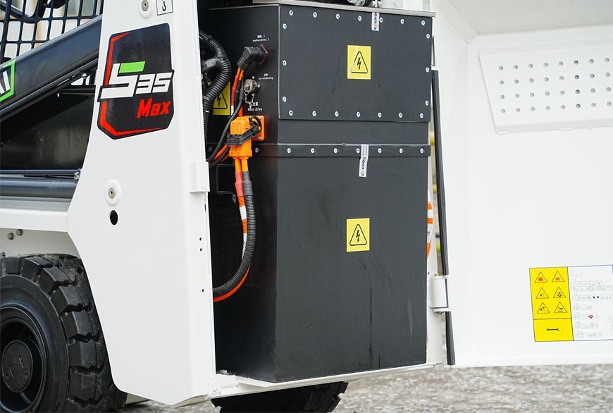 Black battery pack YUCHAI S25 in a white skid steer, with hazard warning labels.