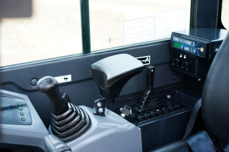 Intérieur de la cabine d'un véhicule avec commandes : levier de vitesses, joystick et panneau d'affichage.