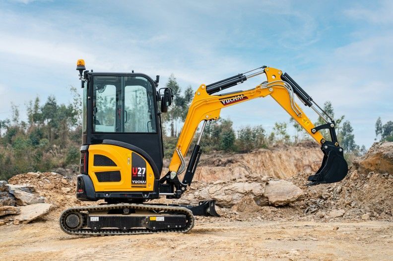 Une mini-pelle jaune et noire sur un chantier de construction, en train de creuser un tas de terre.
