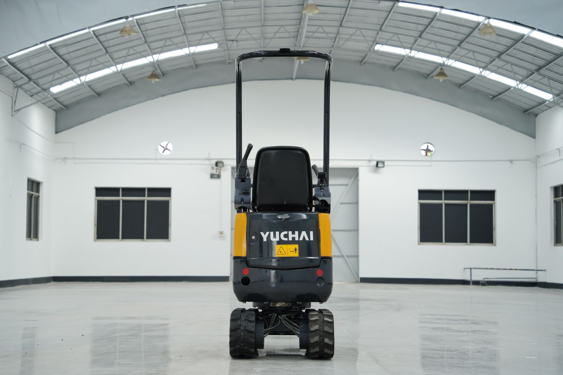 Vue arrière d'une mini-pelle YUCHAI jaune et noire à l'intérieur d'un bâtiment industriel blanc.